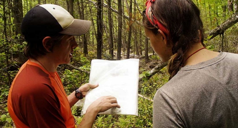 two people examine a piece of paper in a wooded area